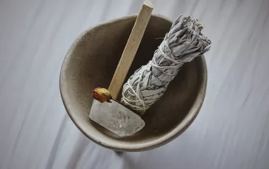 a smudge stick, wood, and a quartz crystal in a bowl.