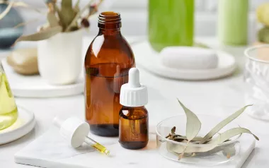 a bottle of essential oil, a dropper, a cup, and a bundle of sage on a table.