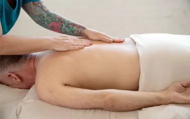 An MT with a vibrant tattoo sleeve lays two flat hands on a client's back.