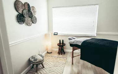an empty massage room with a wooden table and decor on the wall. the window is open. 