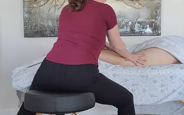 author Cindy Williams sits on a stool, balancing her weight with both feet on the ground as she provides massage to a client's leg..