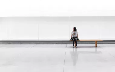 a woman sits on a long bench in an empty room.