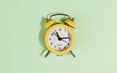 an analog alarm clock against a pale mint-green background.