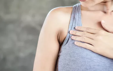 a white woman in a tank top holds a spot on her chest.