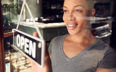 Black woman with short hair changes a business open sign in the window.