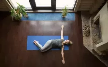 A woman lies on a blue yoga mat on the floor with her arms outstretched.