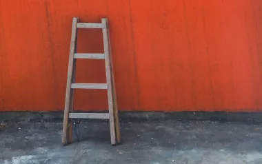 A wooden ladder leans against a red wall.