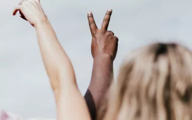One person with white skin tone and another with dark skin tone make peace signs with their hands.