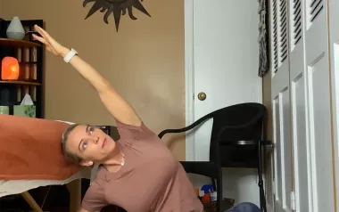 Author Marisa Savino performs a side-bend stretch yoga pose while seated on the floor.