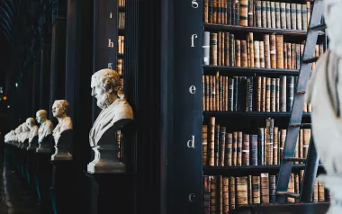 A large, dark library with rows of books and busts of historical figures.