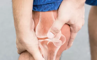 Person in shorts clutching their knee with a see-through overlay of the leg bones and joints underneath.
