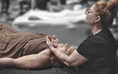 Woman gives massage to client lying supine on massage table. 