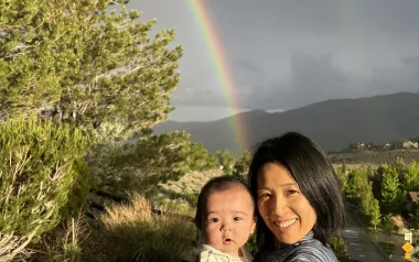 Kei Yumoto and child standing outside with a rainbow in the background.