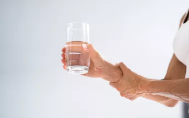 A person holding a glass of water and steading their arm.