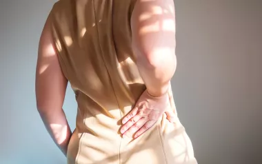 A person in a beige dress holds a hand to their lower back.