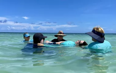 Group of massage therapists support a female client floating in the ocean.