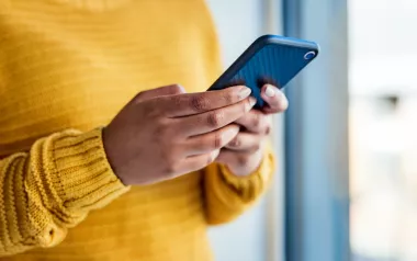 A person in a yellow sweater holding their smartphone with both hands.