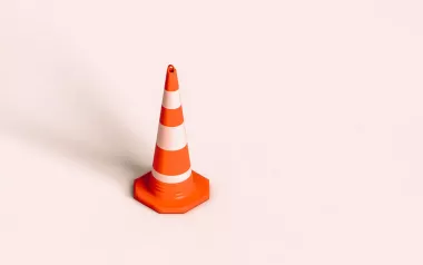 A traffic cone stands by itself on a pink floor.