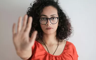 A woman with glasses stands with her arm outstretched in a "stop" gesture.