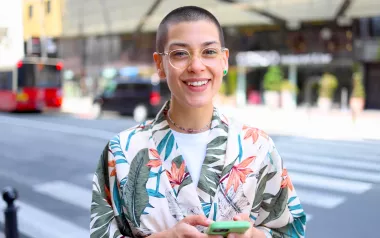 A smiling young adult stands on a street corner.