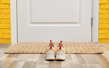 A pair of shoes sits in front of a door and welcome mat.