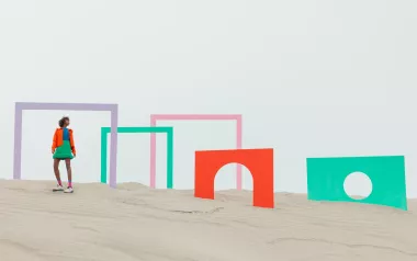 A woman standing on a beach with colorful door frames near her.