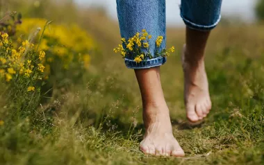 A pair of feet walk through a field with little flowers tucked into the cuff of their jeans.