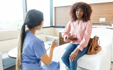 A Black female client points to her stomach in discussion with a therapist.