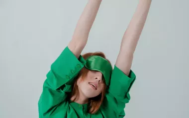 A woman wearing an eye mask stretches her arms upward.