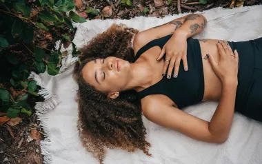 A woman lies on a blanket on the ground and practices breathwork.