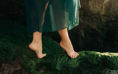 A dancer on their toes walks on a mossy bed.