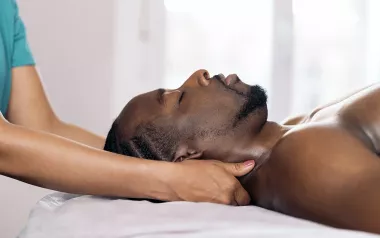 A massage therapist works on a Black man's head and neck area.