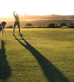 A golfer starts his backswing as the sun sets behind him.