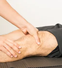 A massage therapist works on a client's knee area.