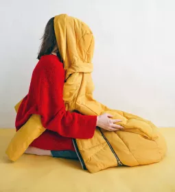 A woman kneels with a jacket covering her face.