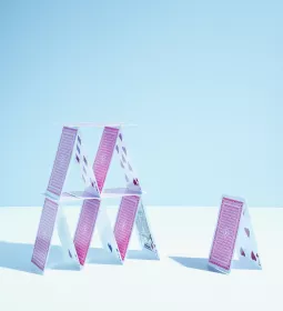 A tall tower of multiple playing cards stands next to a smaller tower of two playing cards.