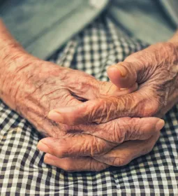 elderly woman sitting with hands folded in lap.