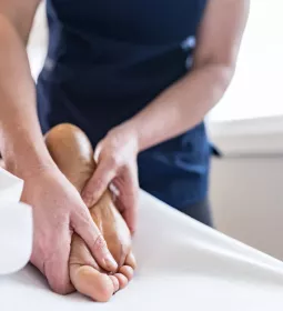 Massage therapist massaging bottom of client's foot.