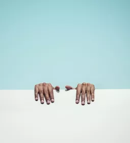 two hands grip a white ledge behind a blue background.