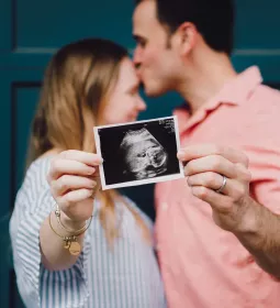 a male and female couple kiss while they hold up an ultrasound photo of a baby.