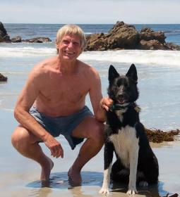Art Riggs on Carmel Beach in Monterey County, California, smiling with his dog.