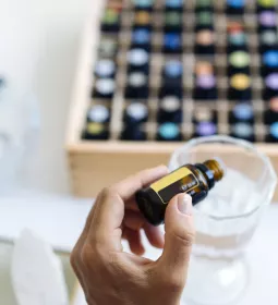 a large selection of small bottles of essential oils, with one being added to a cup.