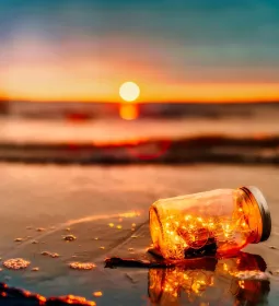 yellow string lights in a jar, floating on a beach at sunset.