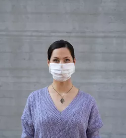 a woman in a purple sweater wears a disposable face mask.
