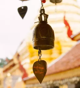 a metal bell hangs outside a gold and yellow wat temple in Thailand.