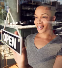 Black woman with short hair changes a business open sign in the window.