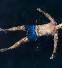 a person in blue swim shorts floats in a dark pool on their back.