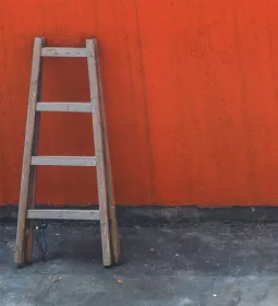 A wooden ladder leans against a red wall.