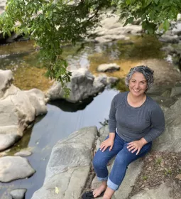 A professional portrait of Kerry Jordan sitting by a creek.