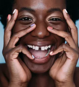 Black woman with wide smile holding her face with her hands. 